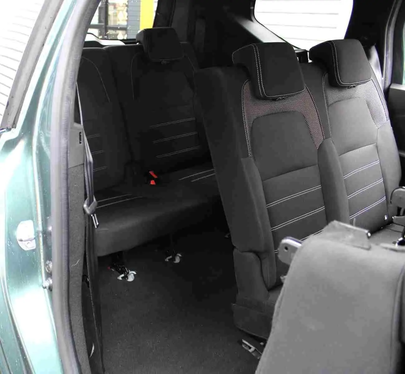 Vue intérieure arrière droite du Dacia Jogger vert cèdre, montrant les sièges en tissu noir avec surpiqûres claires.