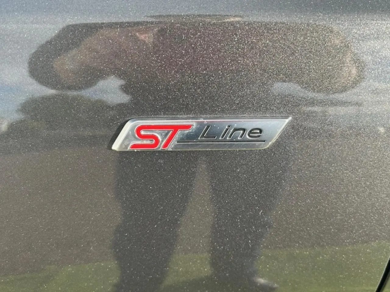 Gros plan sur le badge ST-Line rouge et noir sur la carrosserie gris metallic d'une Ford Focus IV.