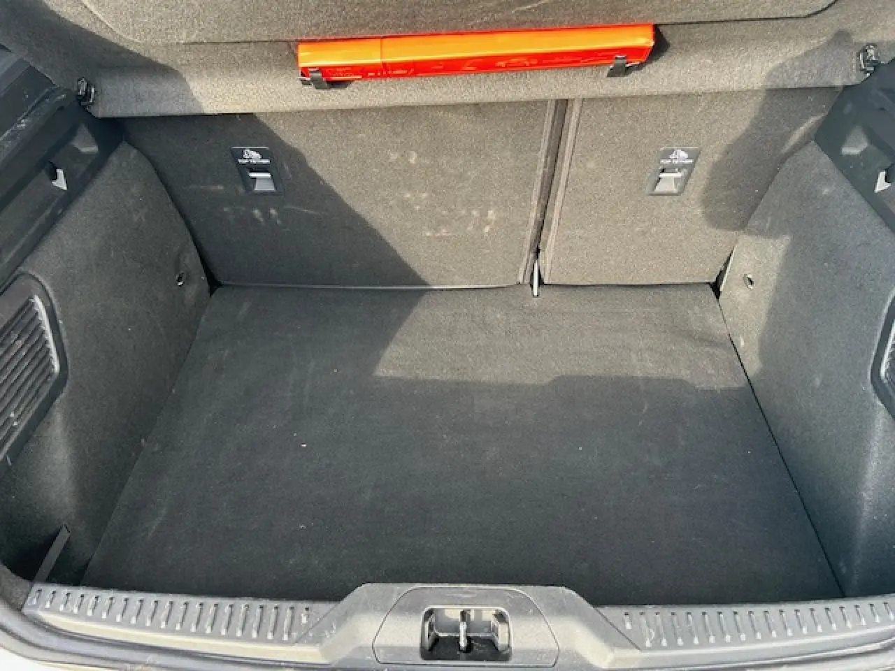 Vue plongeante sur le coffre spacieux et propre de la Ford Focus IV gris Magnetic Metal, avec tapis noir et rangement intégré.