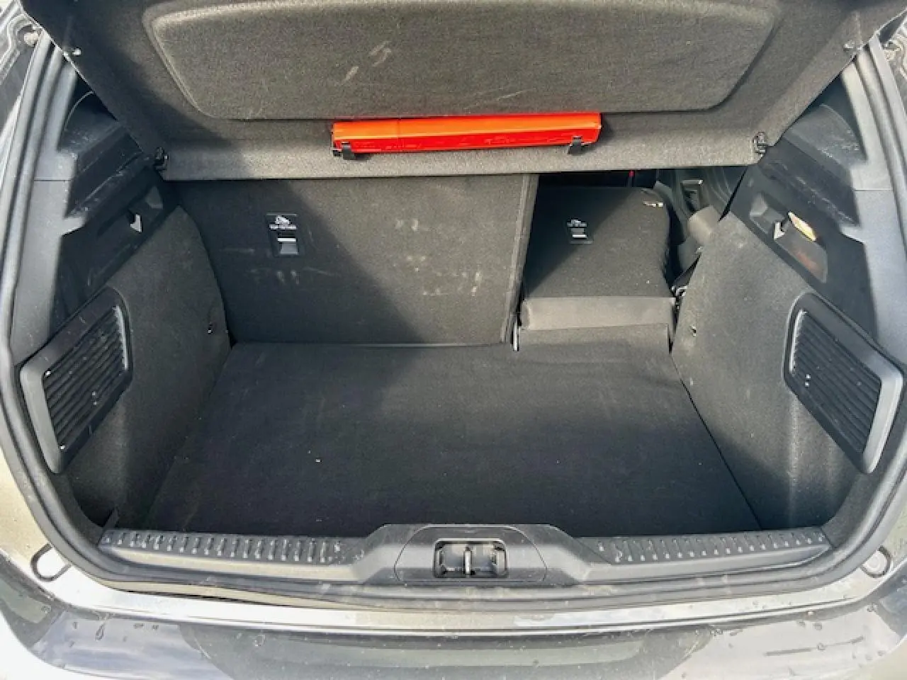 Coffre ouvert vu de l'arrière de la Ford Focus IV gris Magnetic, banquette arrière rabattue partiellement côté droit.