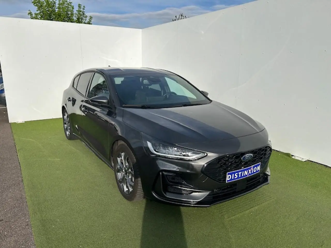 Ford Focus IV ST-Line X gris métallisé vue 3/4 avant avec calandre noire et jantes alliage 17 pouces.