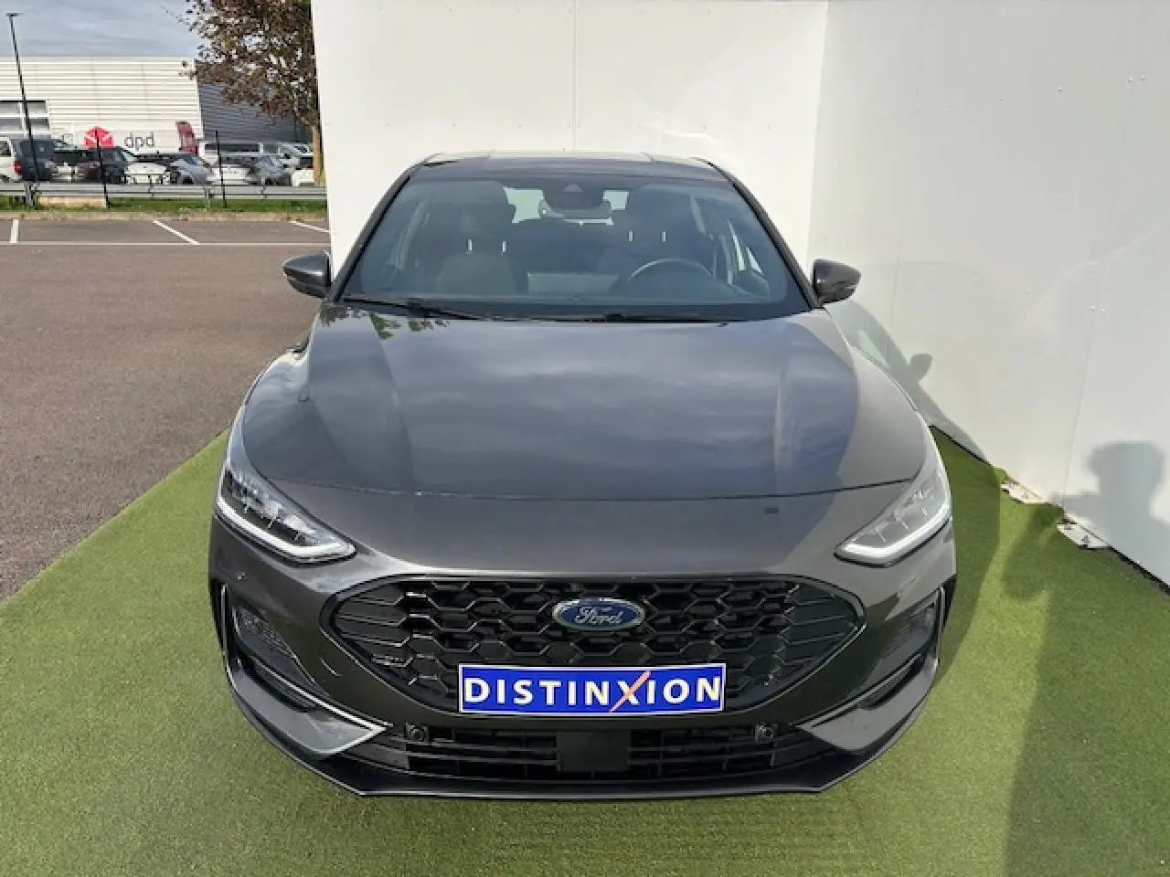 Ford Focus IV ST-Line X gris métallisé vue de face avec calandre noire et plaques Distinxion sur sol vert.