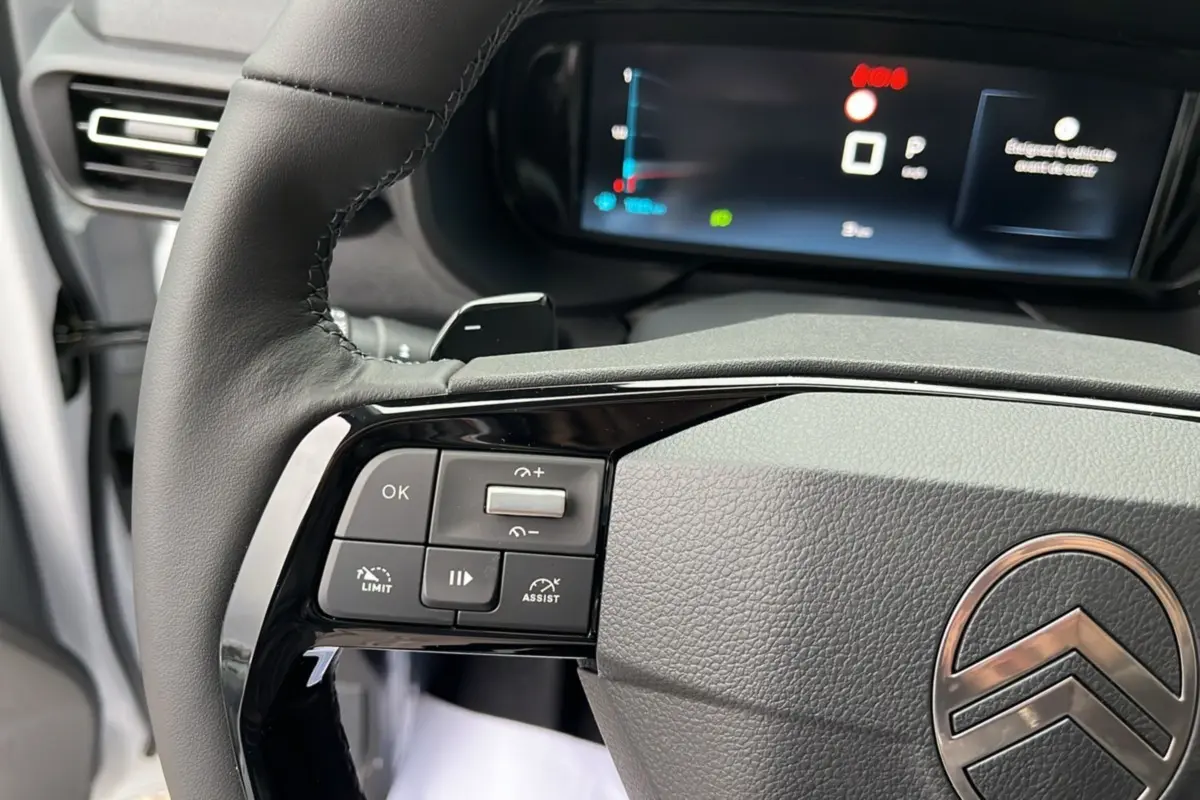 Gros plan sur le volant cuir multifonctions gris du Citroën Berlingo 2025 avec commandes intégrées et tableau de bord numérique flou.