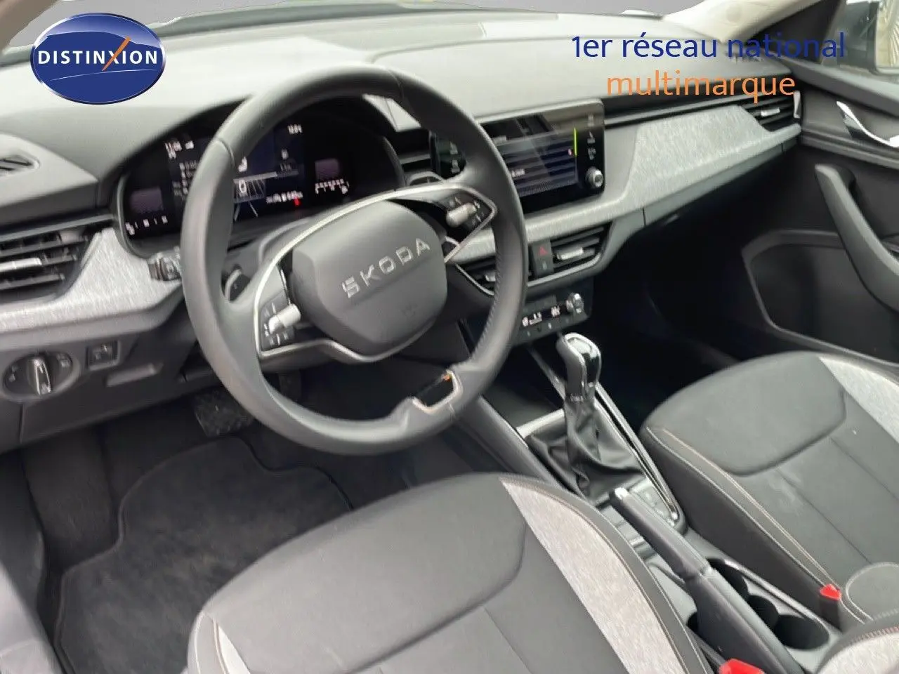 Vue intérieure côté conducteur du Skoda Kamiq 2025, volant multifonction, sièges tissu noir et gris, console centrale avec boîte auto.
