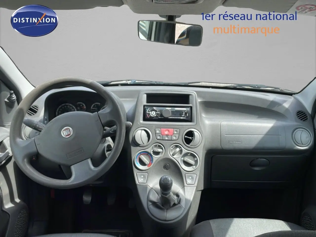 Vue frontale de l'habitacle de la Fiat Panda blanche, mettant en valeur le tableau de bord et la boîte manuelle.