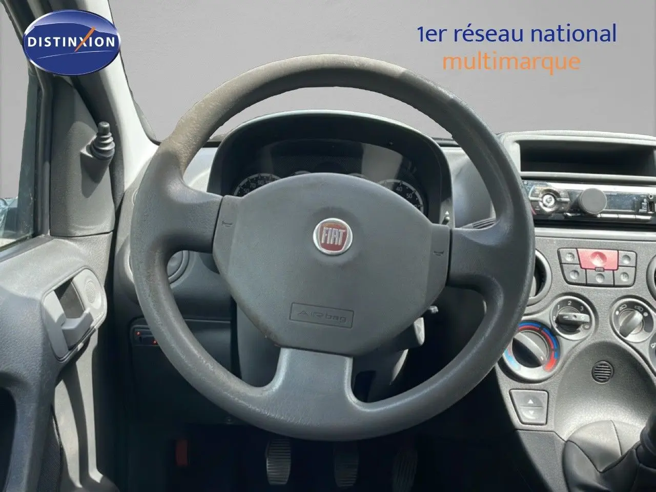 Vue intérieure centrée sur le volant gris de la Fiat Panda blanche, avec tableau de bord et commandes visibles.
