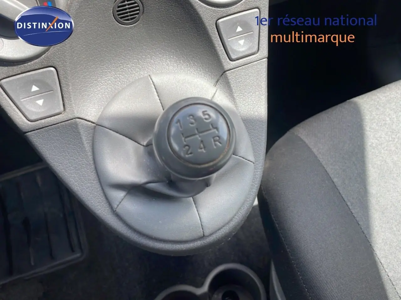Gros plan sur le levier de vitesses manuel noir de la Fiat Panda blanche, avec siège tissu gris visible à droite.