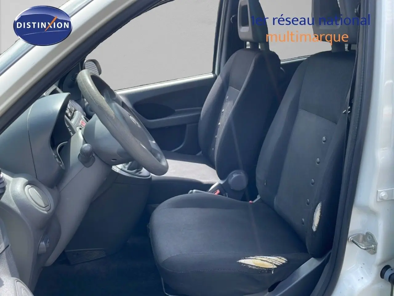 Vue intérieure côté conducteur d'une Fiat Panda blanche de 2011, sièges noirs usés avec déchirures visibles.
