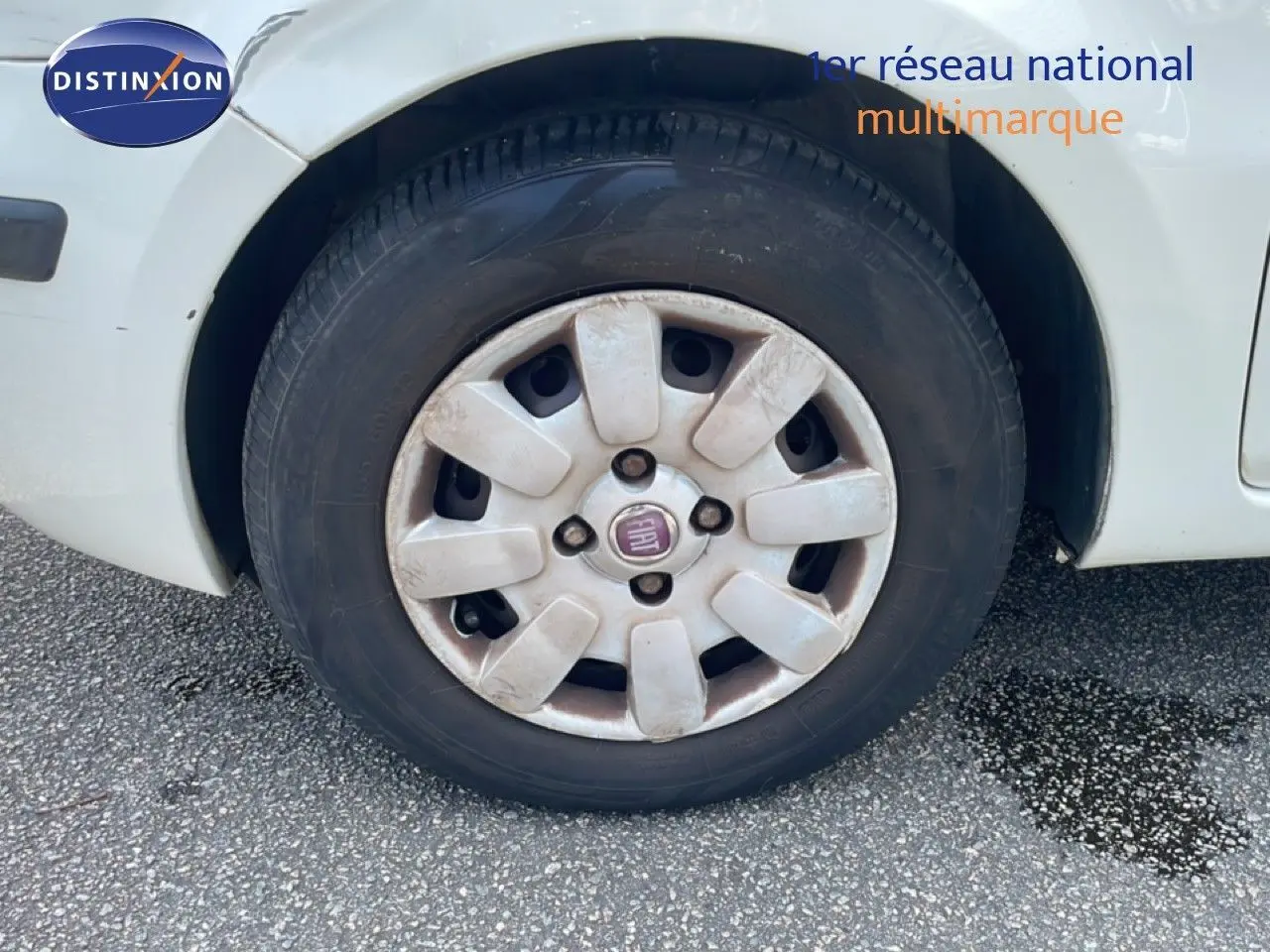 Gros plan sur la roue avant gauche blanche d'une Fiat Panda 2011 avec jante en plastique et logo Fiat au centre.