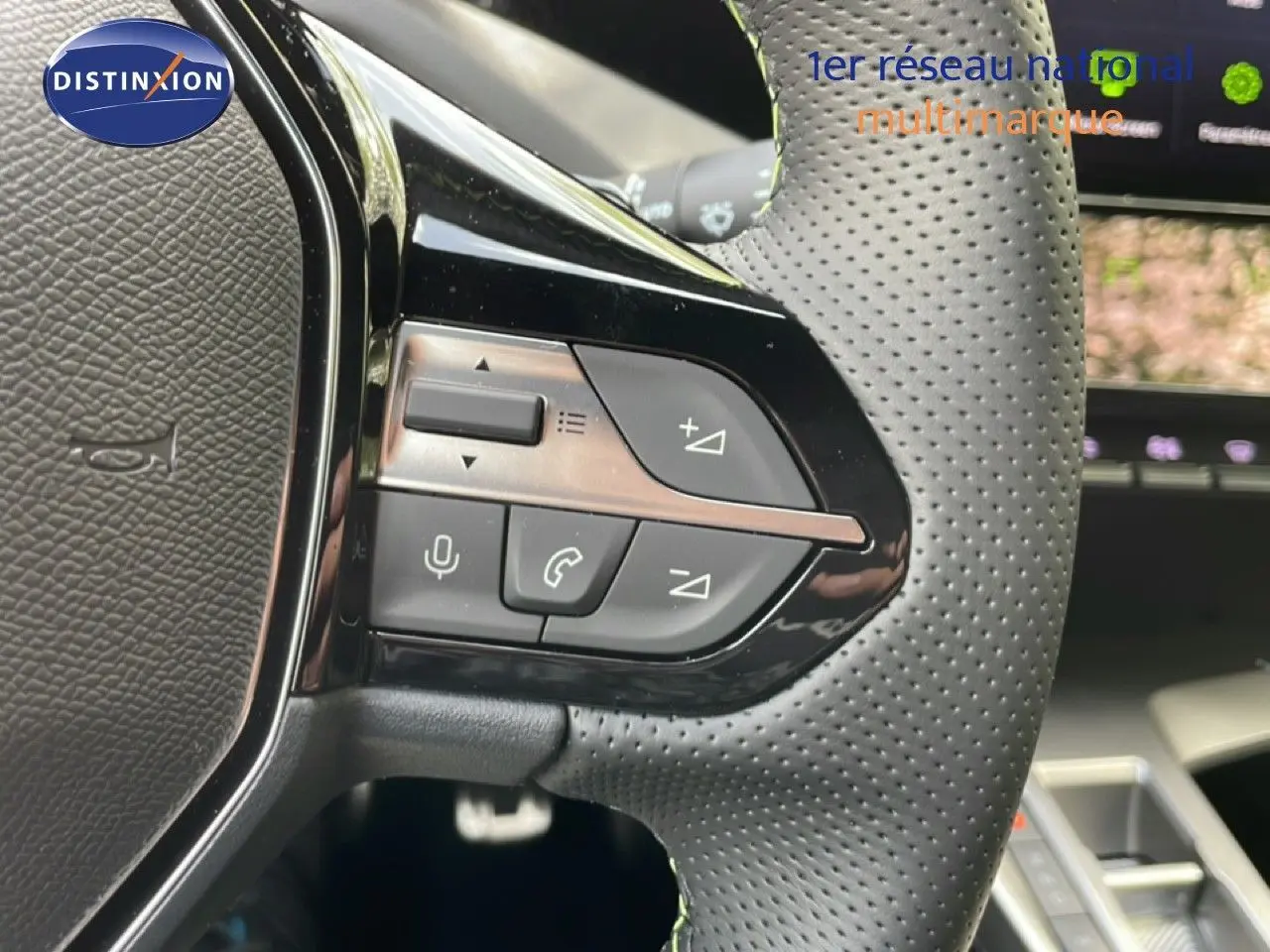 Gros plan sur les commandes au volant en cuir perforé noir de la Peugeot 308 gris Artense, intérieur moderne et connecté.