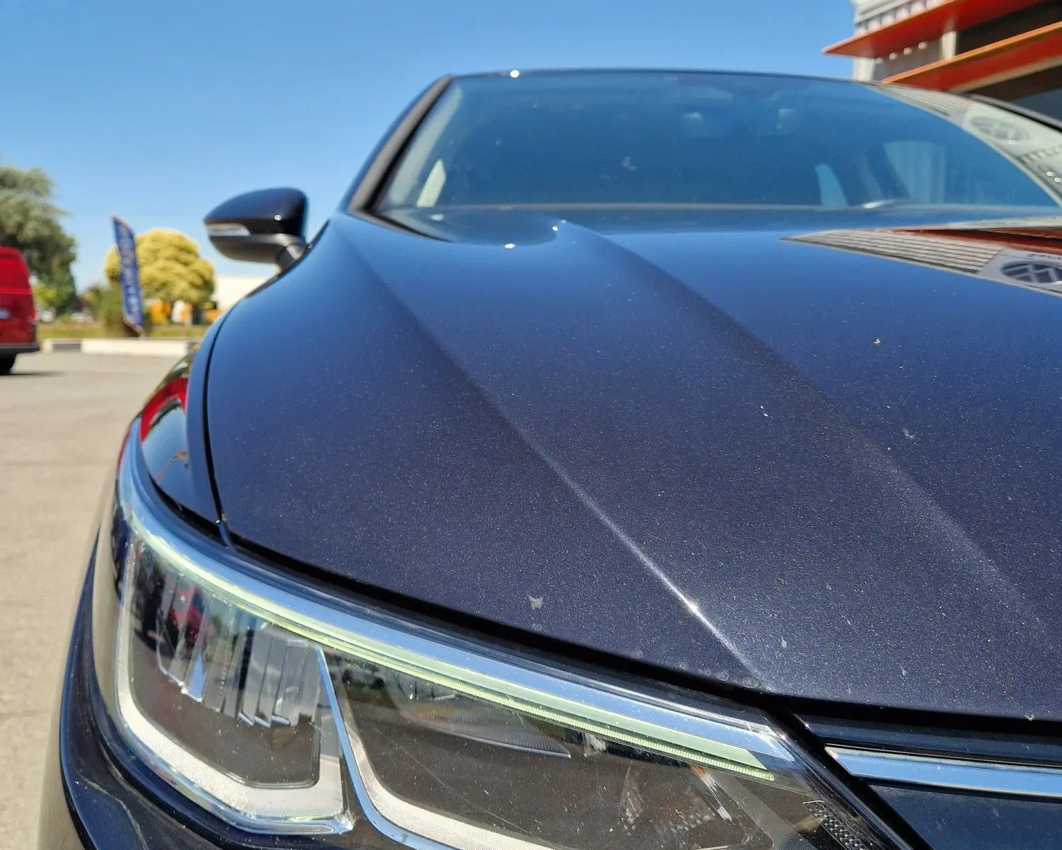 Gros plan sur le phare avant gauche d'une Volkswagen Golf VIII noire métal sous un ciel bleu clair.