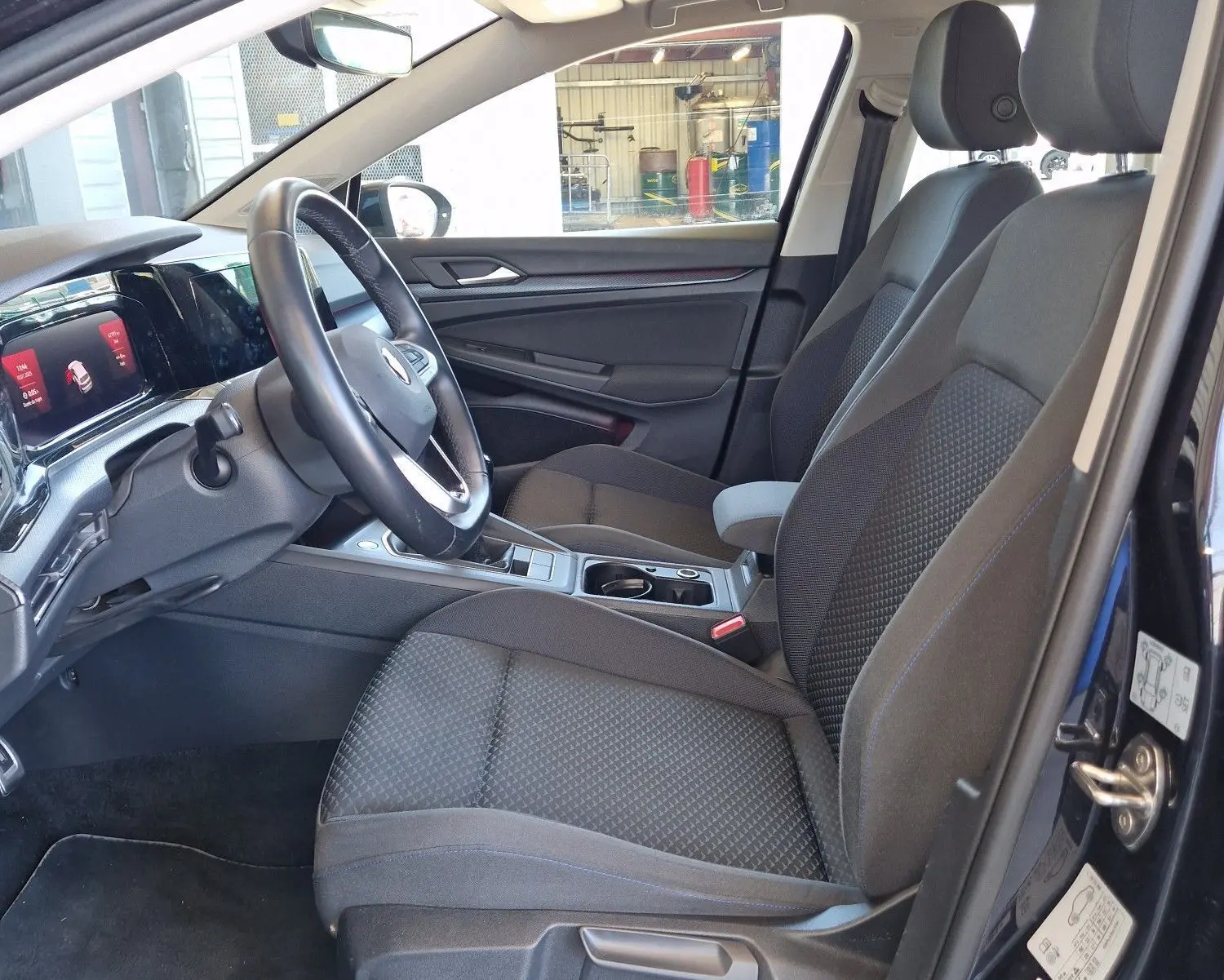 Intérieur de la Volkswagen Golf VIII 2.0 TDI noir métal, vue côté conducteur avec sièges tissu gris et tableau de bord moderne.