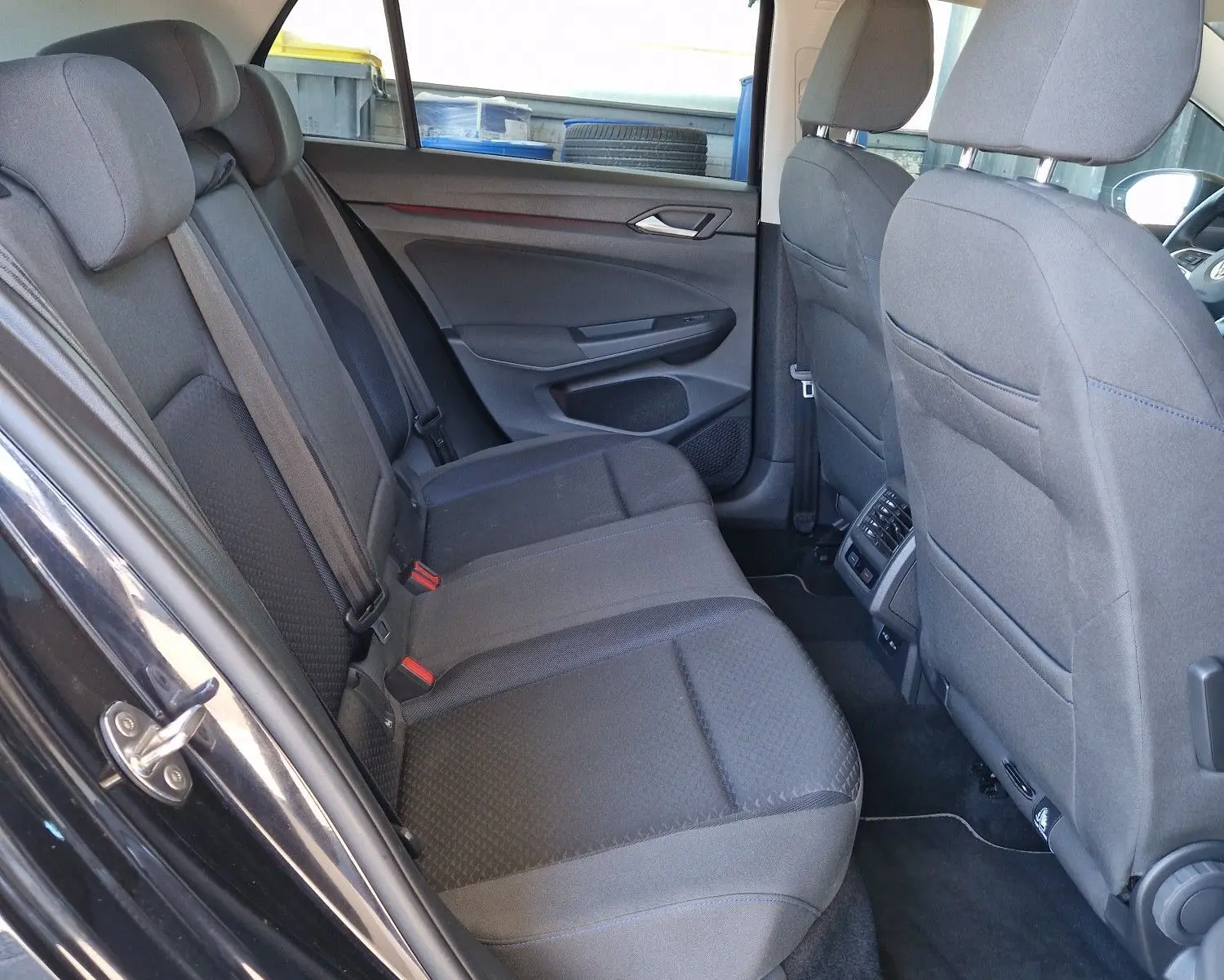 Vue intérieure côté gauche des sièges arrière gris tissu de la Volkswagen Golf VIII noire métal, avec portières ouvertes.