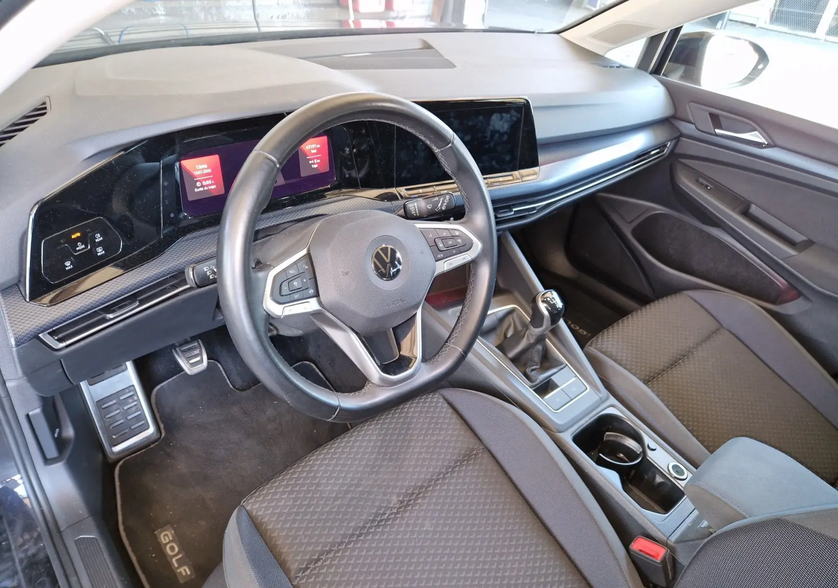 Intérieur avant droit de la Volkswagen Golf VIII noire, volant multifonction, tableau de bord numérique et boîte manuelle.