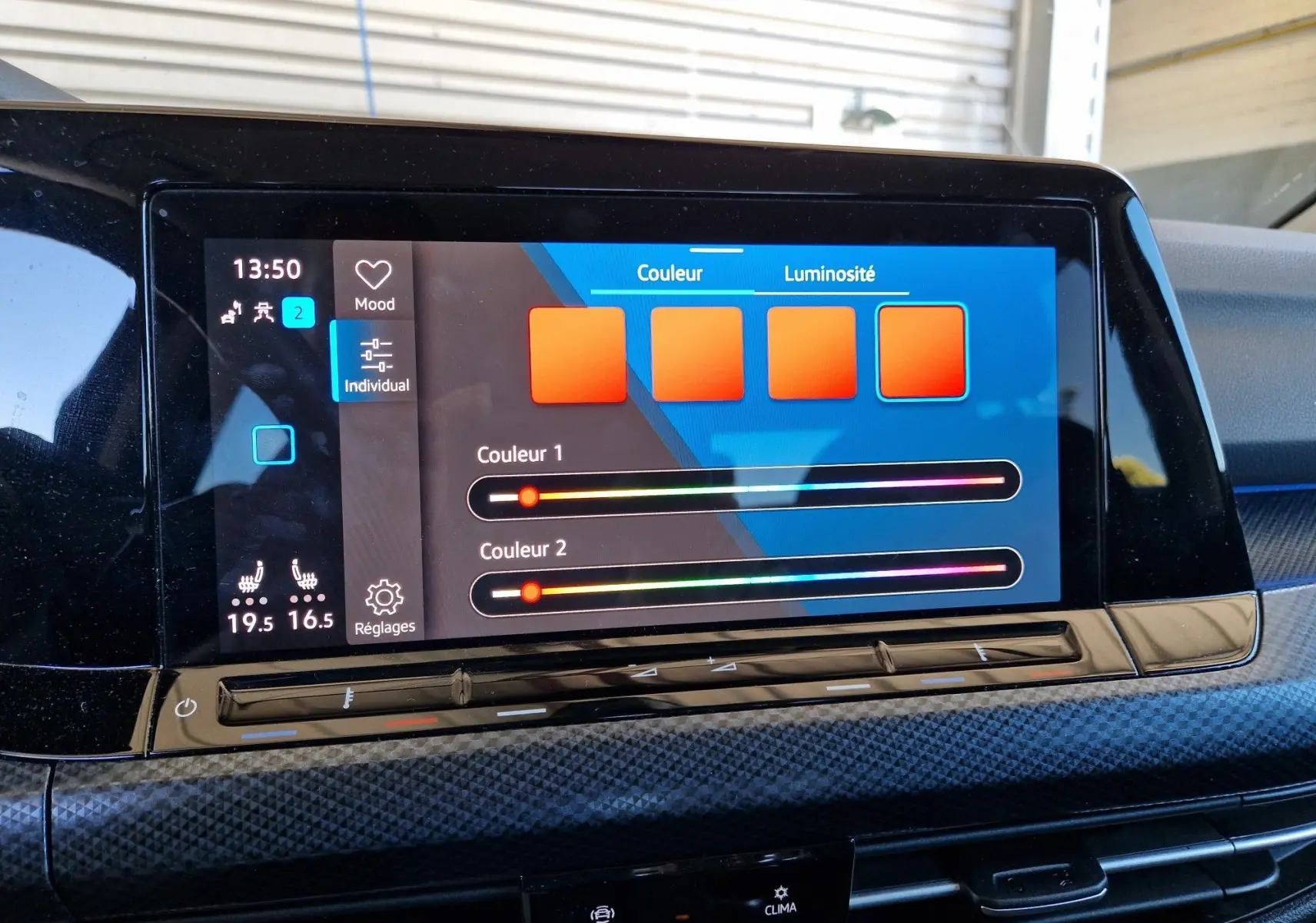 Écran tactile central de la Volkswagen Golf VIII noir métal, affichant les réglages de couleur et luminosité de l'ambiance intérieure.