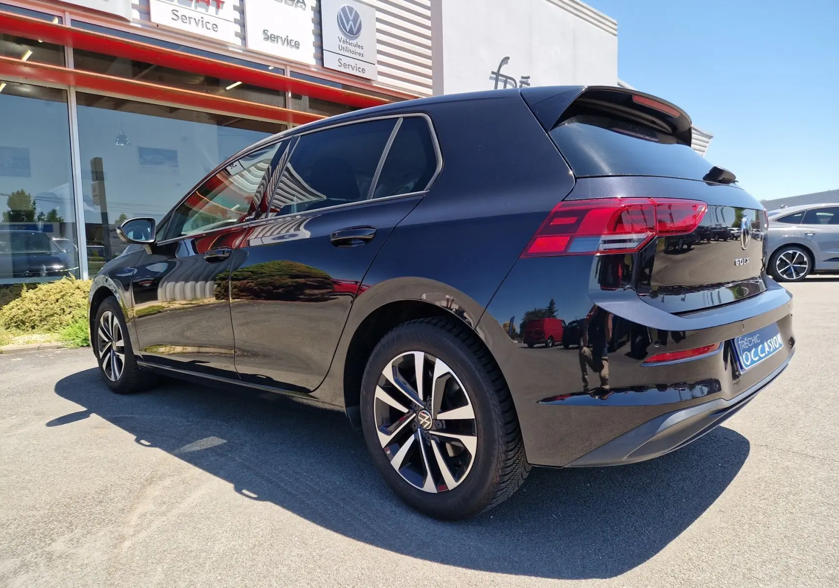 Vue 3/4 arrière droite d'une Volkswagen Golf VIII noire métallisée, avec jantes alliage et vitres teintées, stationnée en extérieur.