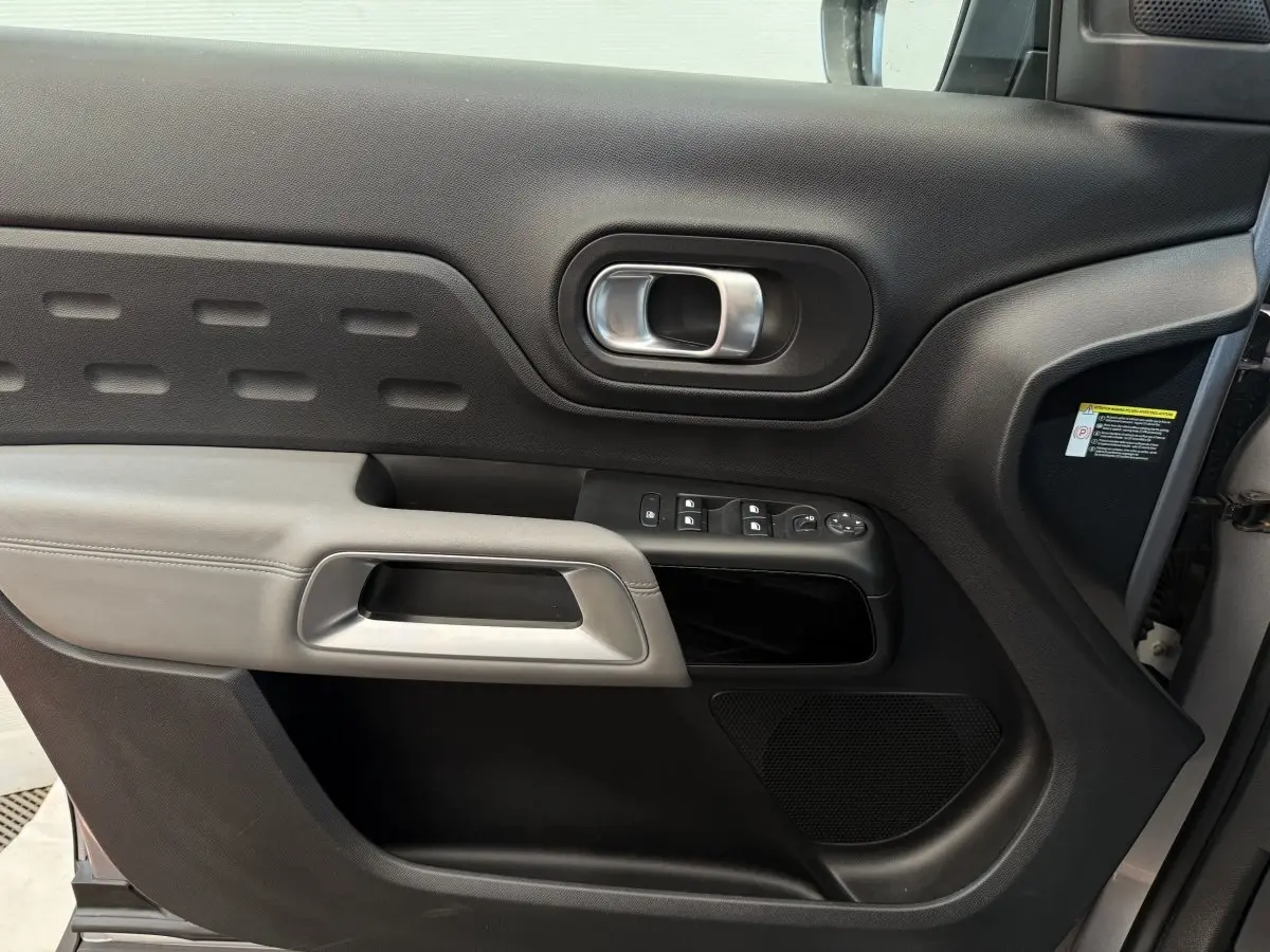 Vue intérieure côté gauche de la porte avant gris clair du Citroën C5 Aircross avec commandes de vitres et poignée argentée.