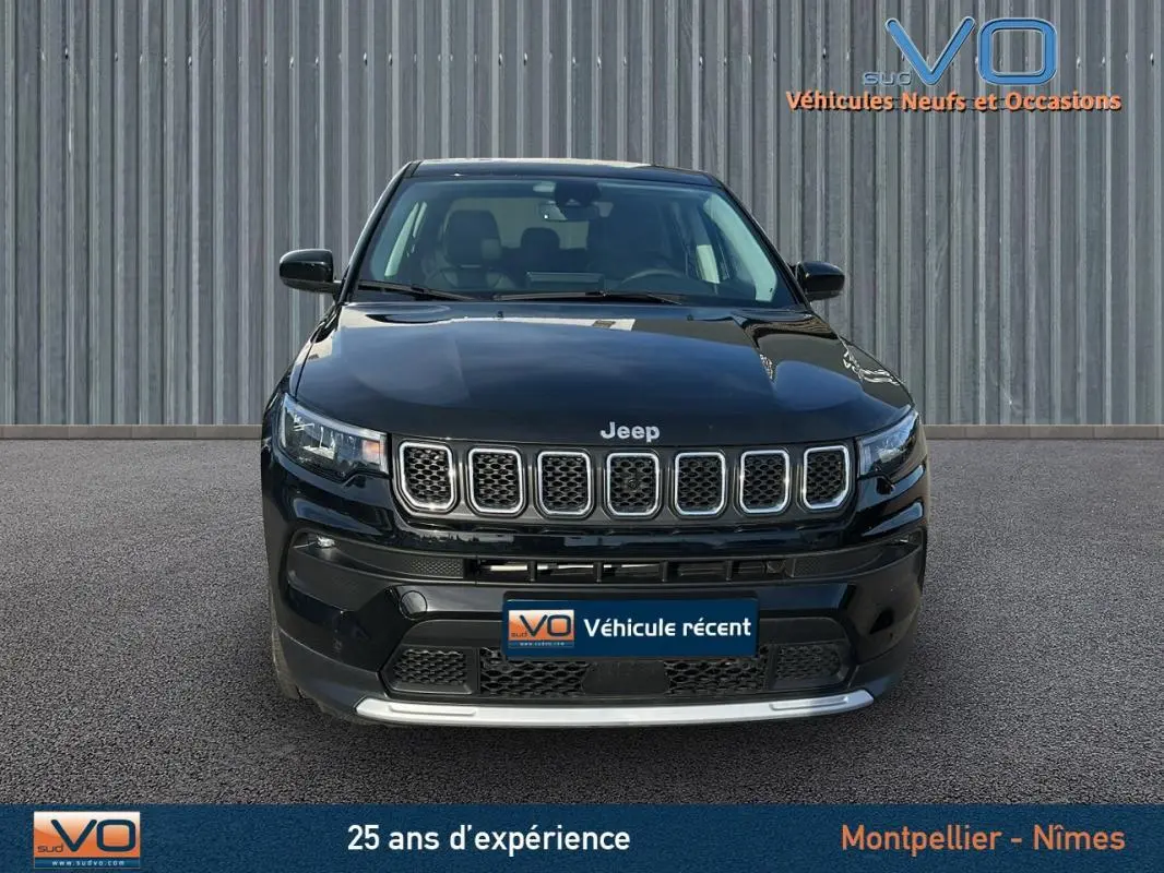 Vue avant d'un Jeep Compass noir 2024 avec calandre distinctive et phares LED allumés sur fond urbain.