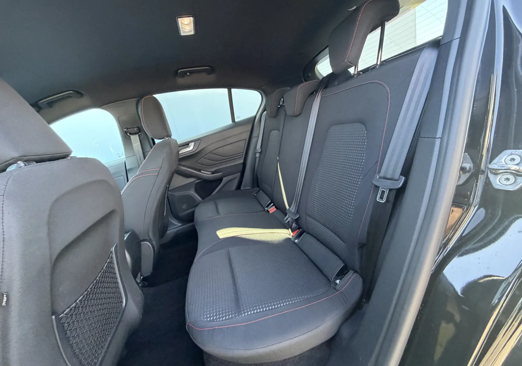 Vue intérieure arrière côté droit de la Ford Focus IV noire Agate, sièges tissu ST-Line avec surpiqûres rouges.