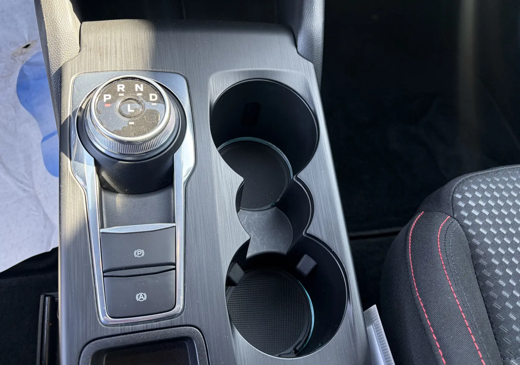 Vue rapprochée de la console centrale noire avec sélecteur rotatif de boîte auto et surpiqûres rouges sur siège tissu Ford Focus IV ST-Line.