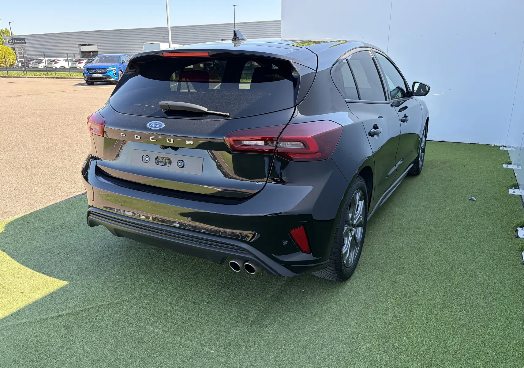 Ford Focus IV noire vue 3/4 arrière droit avec double sortie d’échappement et badges ST-Line visibles.