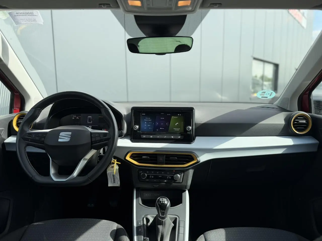 Vue intérieure frontale du poste de conduite du SEAT Arona rouge, avec volant multifonction, écran tactile et détails jaunes autour des aérateurs.