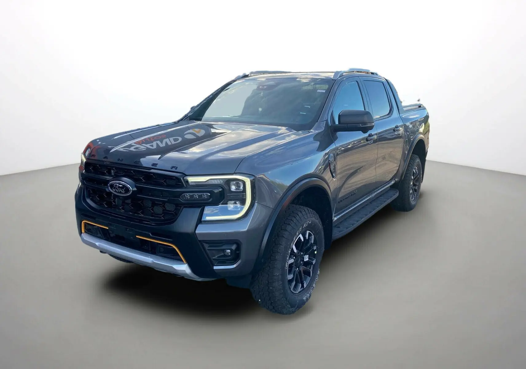 Ford Ranger 205 Wildtrak X Pack X Rideau gris carbone en 3/4 avant avec calandre noire et accents orange.