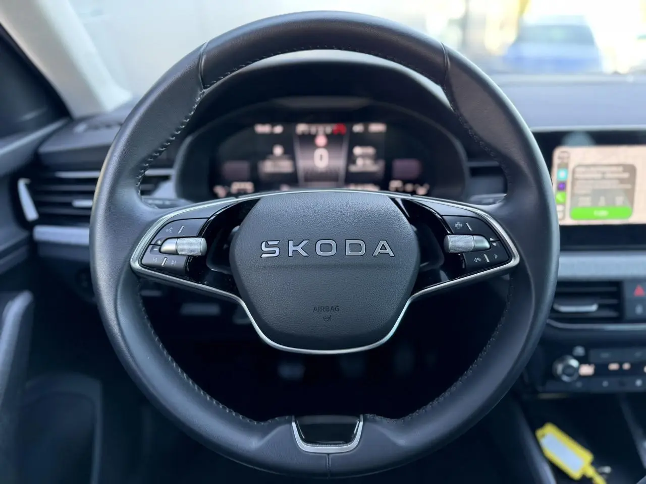 Gros plan sur le volant en cuir noir avec logo SKODA, tableau de bord numérique et écran tactile à droite.