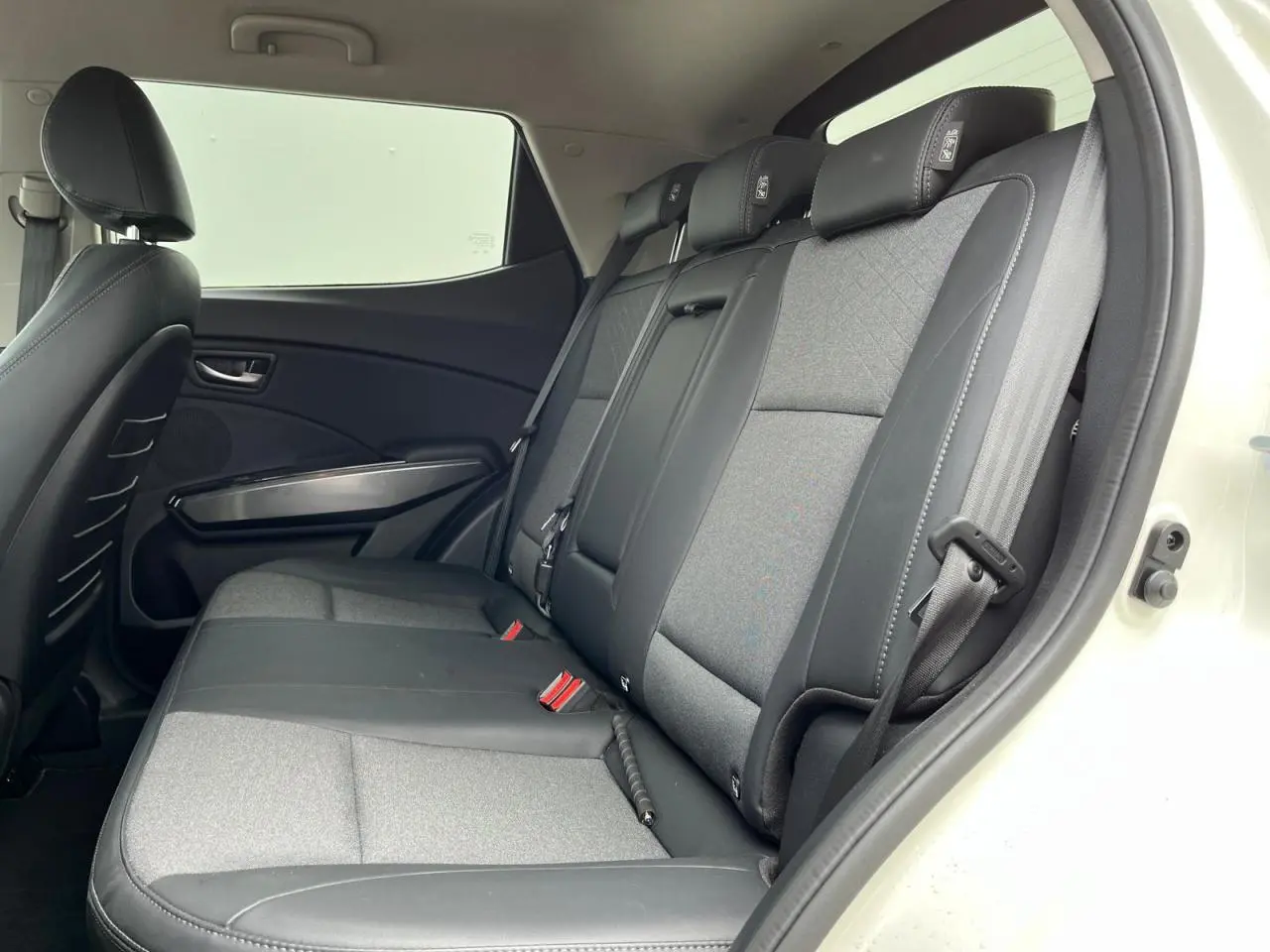 Vue intérieure côté droit des sièges arrière gris et noirs du SsangYong Tivoli blanc, montrant les ceintures et appuie-têtes.
