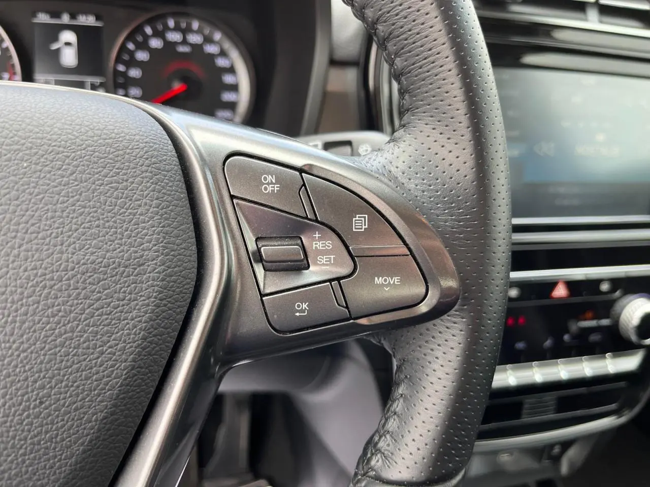 Gros plan sur le volant cuir perforé du SSANGYONG TIVOLI blanc 2021, avec commandes de régulateur de vitesse visibles.