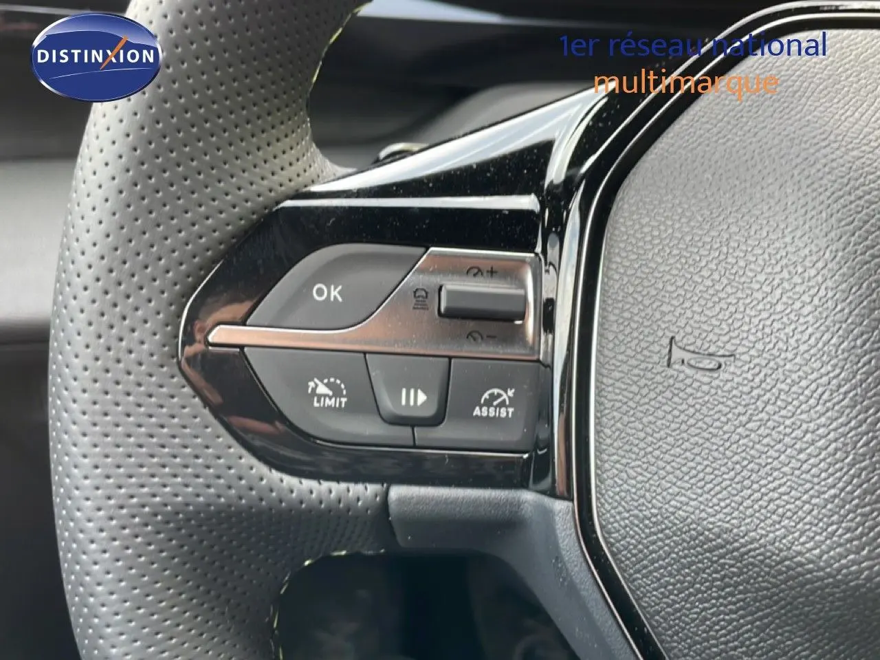 Gros plan sur les commandes gauche du volant en cuir perforé gris d’une Peugeot 308 hybride 2026.