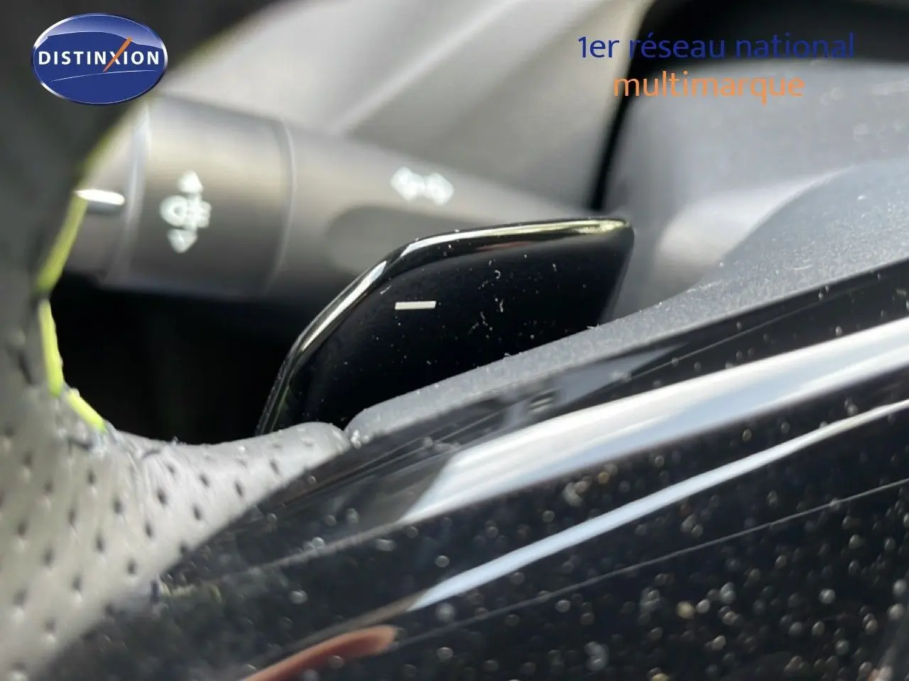 Détail du levier de palettes au volant perforé, intérieur noir de la Peugeot 308 gris Artense hybride 2026.