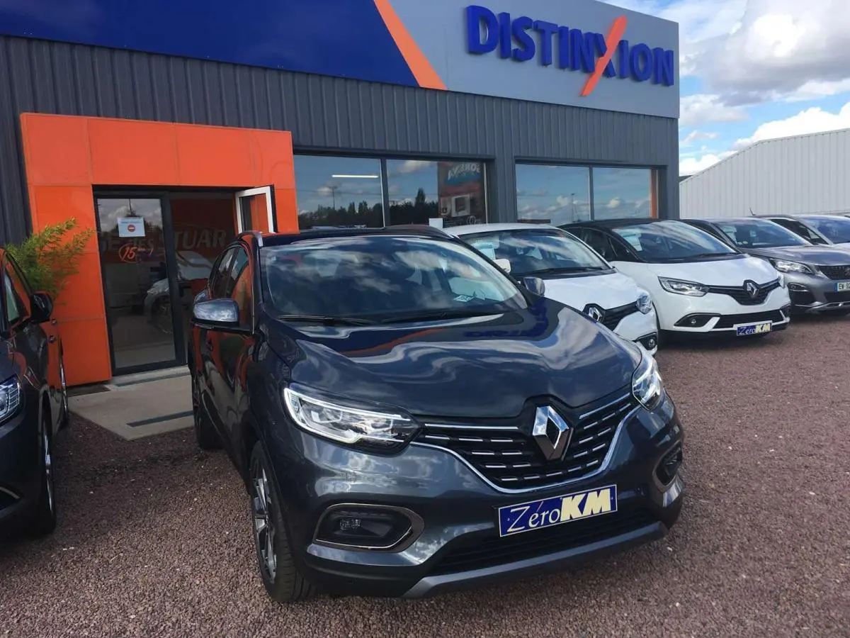Vue 3/4 avant d'un Renault Kadjar gris titanium avec phares LED et jantes alliage 19 pouces devant un concessionnaire.