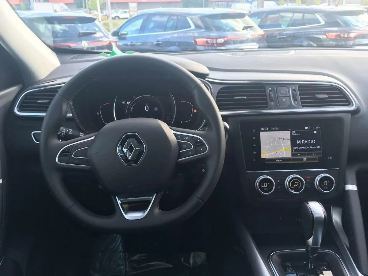 Vue intérieure frontale du tableau de bord du Renault Kadjar gris titanium, avec volant multifonction et écran tactile central allumé.