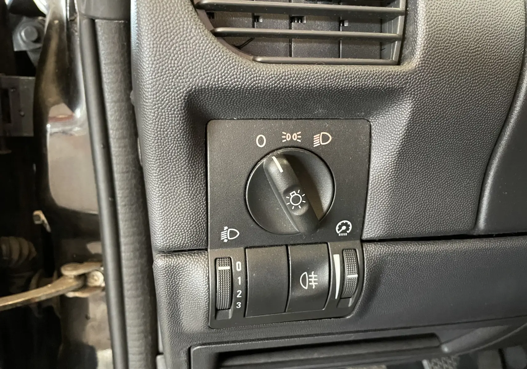 Gros plan sur les commandes d'éclairage intérieures noires du côté gauche d'un Opel Tigra Twintop noir de 2006.