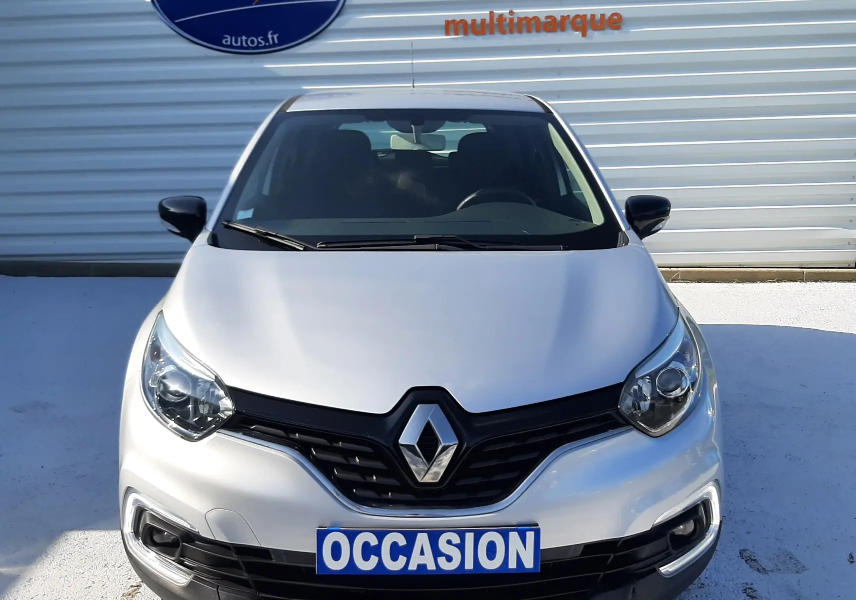 Vue frontale d'un Renault Captur gris platine métal 2019 avec plaque "OCCASION" devant un mur métallique.
