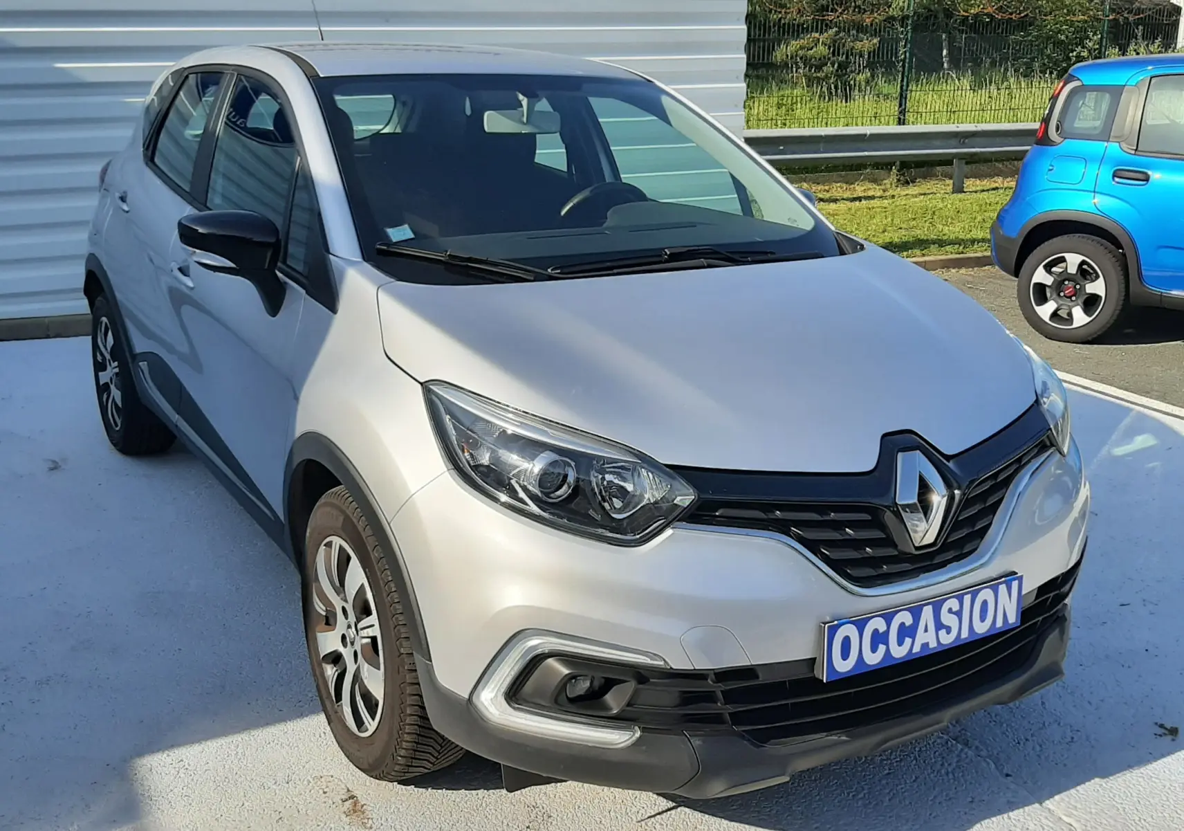 Renault Captur gris platine métal en 3/4 avant droit, avec plaque "OCCASION" et jantes alliage visibles.