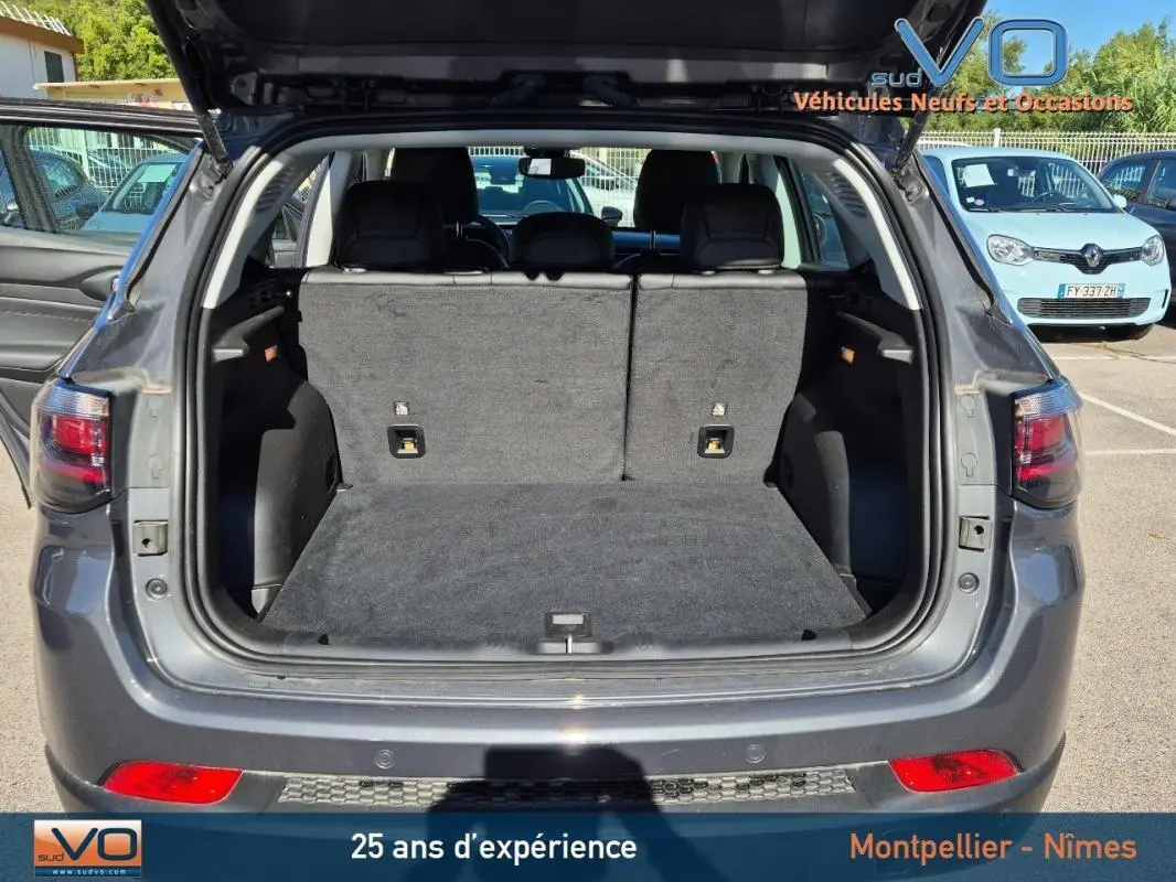 Coffre ouvert d’un Jeep Compass gris 3/4 arrière, montrant l’espace de chargement et les sièges arrière rabattus.