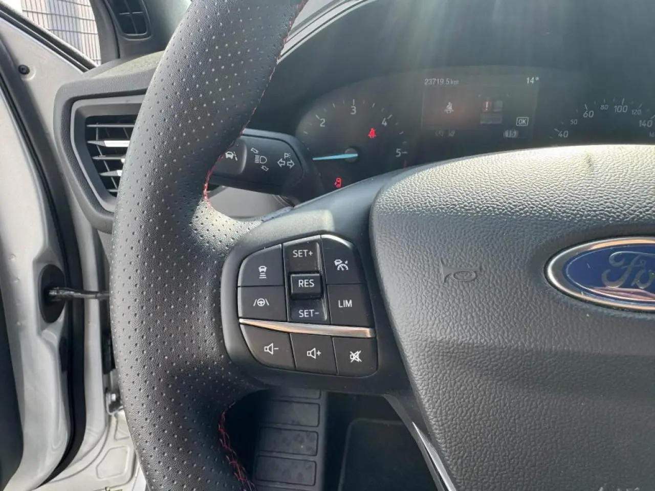 Gros plan sur le volant perforé noir avec surpiqûres rouges et commandes multifonctions de la Ford Focus IV ST-Line.