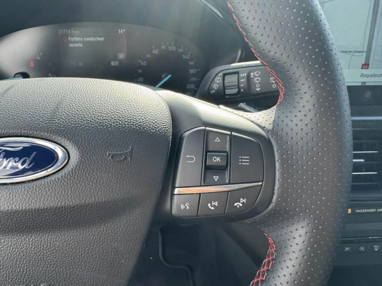 Gros plan sur le volant perforé avec surpiqûres rouges de la Ford Focus IV gris Moondust, affichage numérique visible.