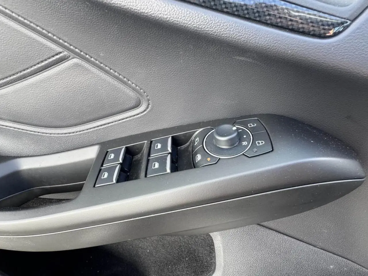 Gros plan sur la commande des vitres et rétroviseurs côté conducteur en plastique noir dans l’habitacle gris du Ford Focus ST-Line.