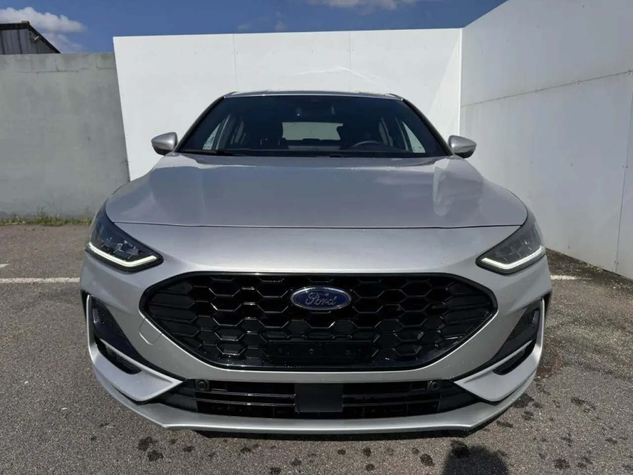 Vue frontale d'une Ford Focus IV ST-Line gris Moondust Metal avec calandre noire hexagonale et phares LED.