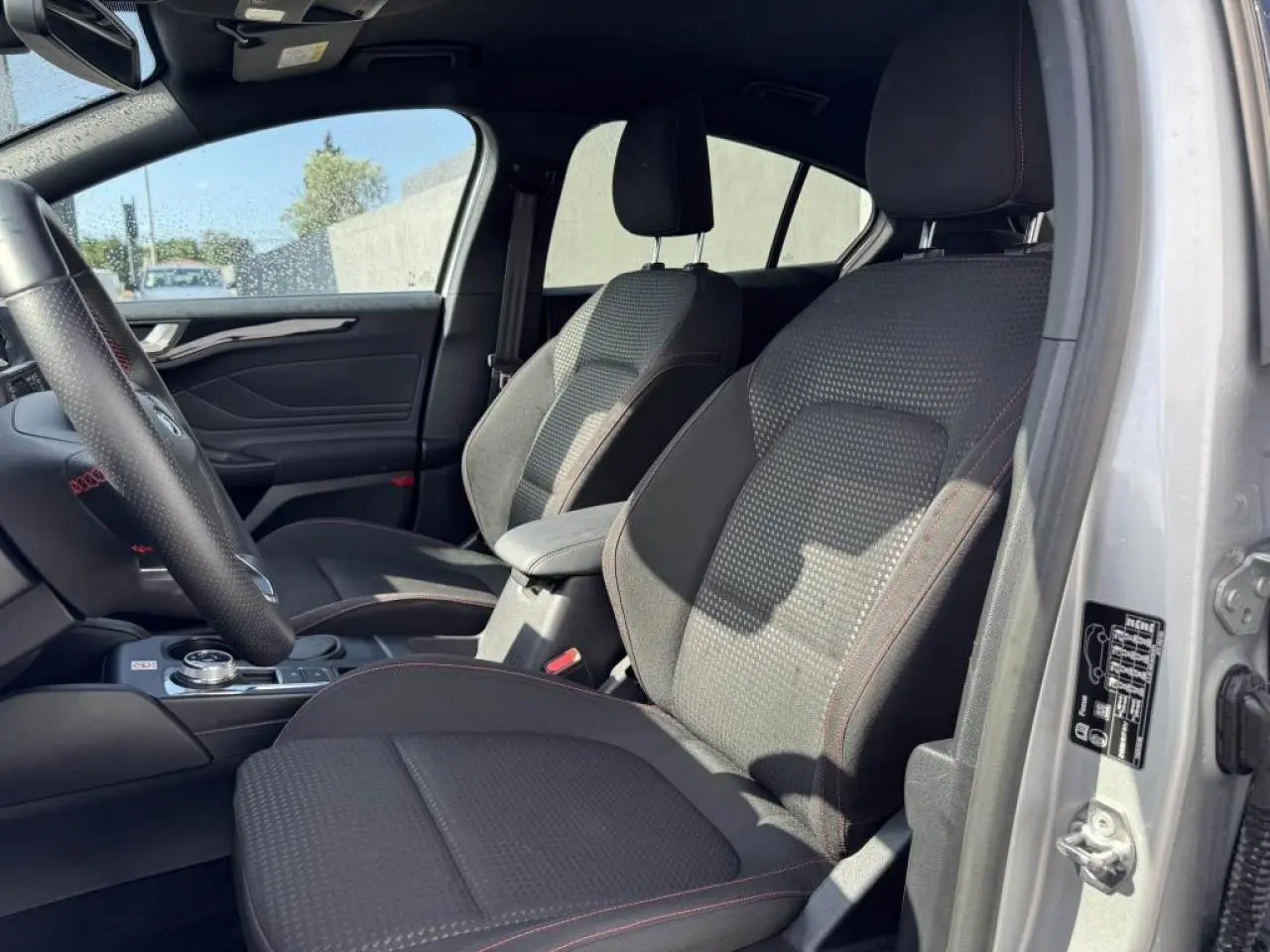 Vue intérieure côté gauche de la Ford Focus IV ST-Line X 2025, sièges tissu gris avec surpiqûres rouges visibles.