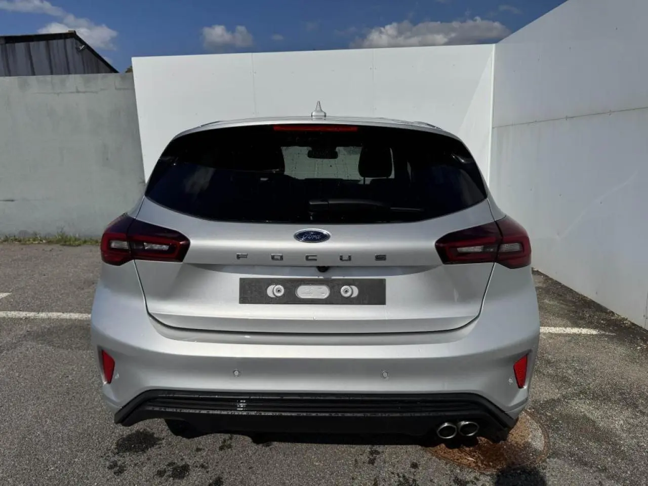 Vue arrière d'une Ford Focus IV gris Moondust Metal avec double sortie d'échappement et feux LED distinctifs.