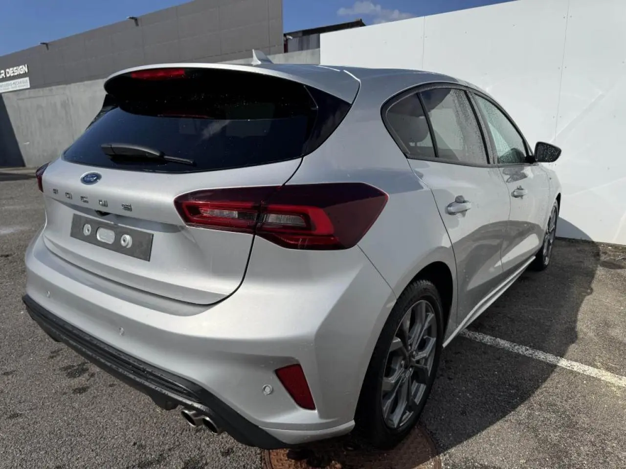 Vue 3/4 arrière droite d'une Ford Focus IV gris Moondust métallisé avec jantes alliage et double sortie d'échappement sport.