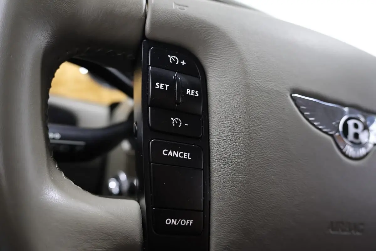 Gros plan sur les commandes de régulateur de vitesse sur le volant beige clair d'une Bentley Continental Flying Spur.