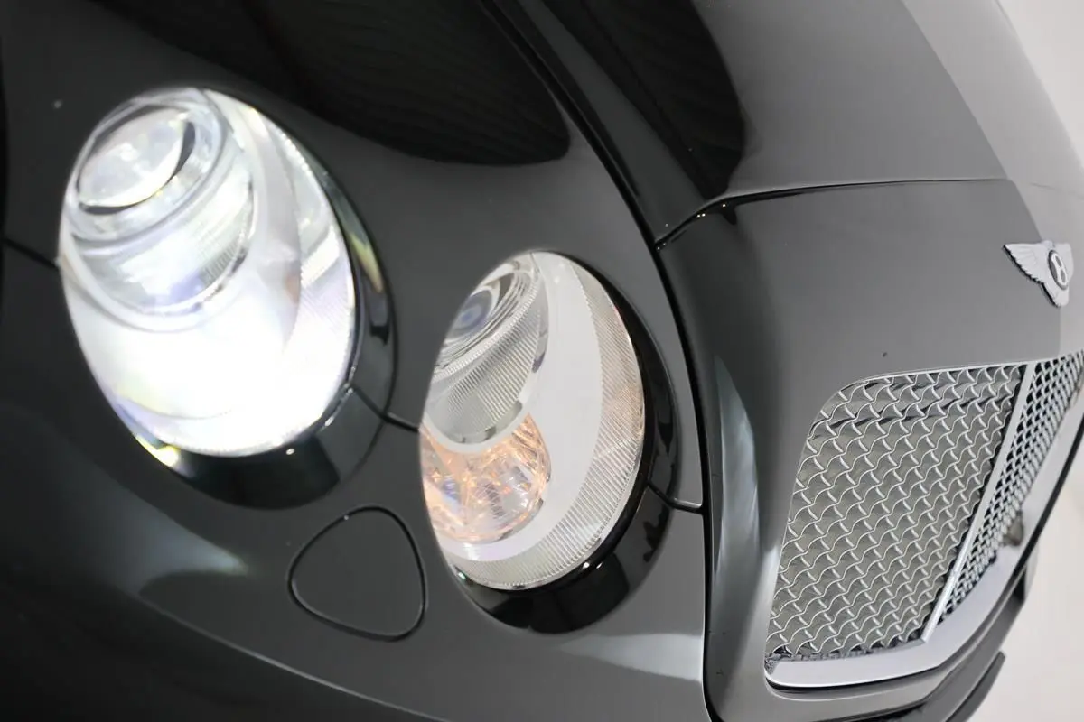 Gros plan sur l'avant droit vert foncé du Bentley Continental Flying Spur, mettant en valeur ses phares ronds et sa calandre chromée.