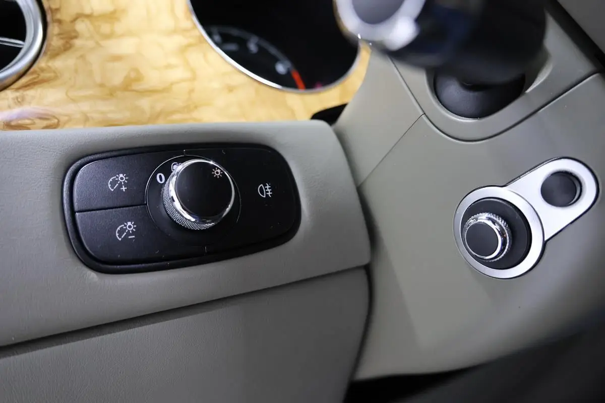 Détail intérieur montrant les commandes d’éclairage sur un tableau de bord beige avec insert bois clair d’une Bentley Continental Flying Spur.