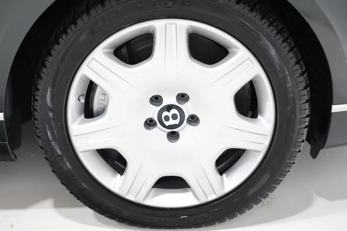 Gros plan sur la jante blanche avec logo Bentley noir, montée sur un pneu noir, partie avant droite du Bentley Continental Flying Spur vert foncé.