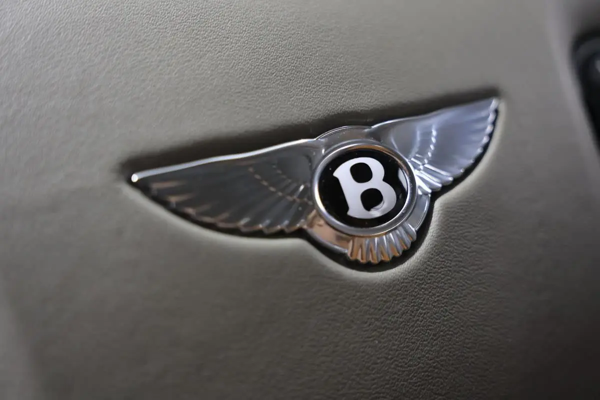 Gros plan sur l'emblème Bentley argenté en forme d'ailes sur fond cuir beige, intérieur d'une Continental Flying Spur.